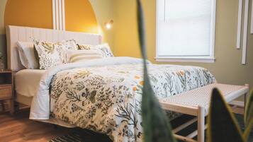 A bedroom with a bed, bedside tables, a window with blinds, and a wall with a curved design and hanging decorations.