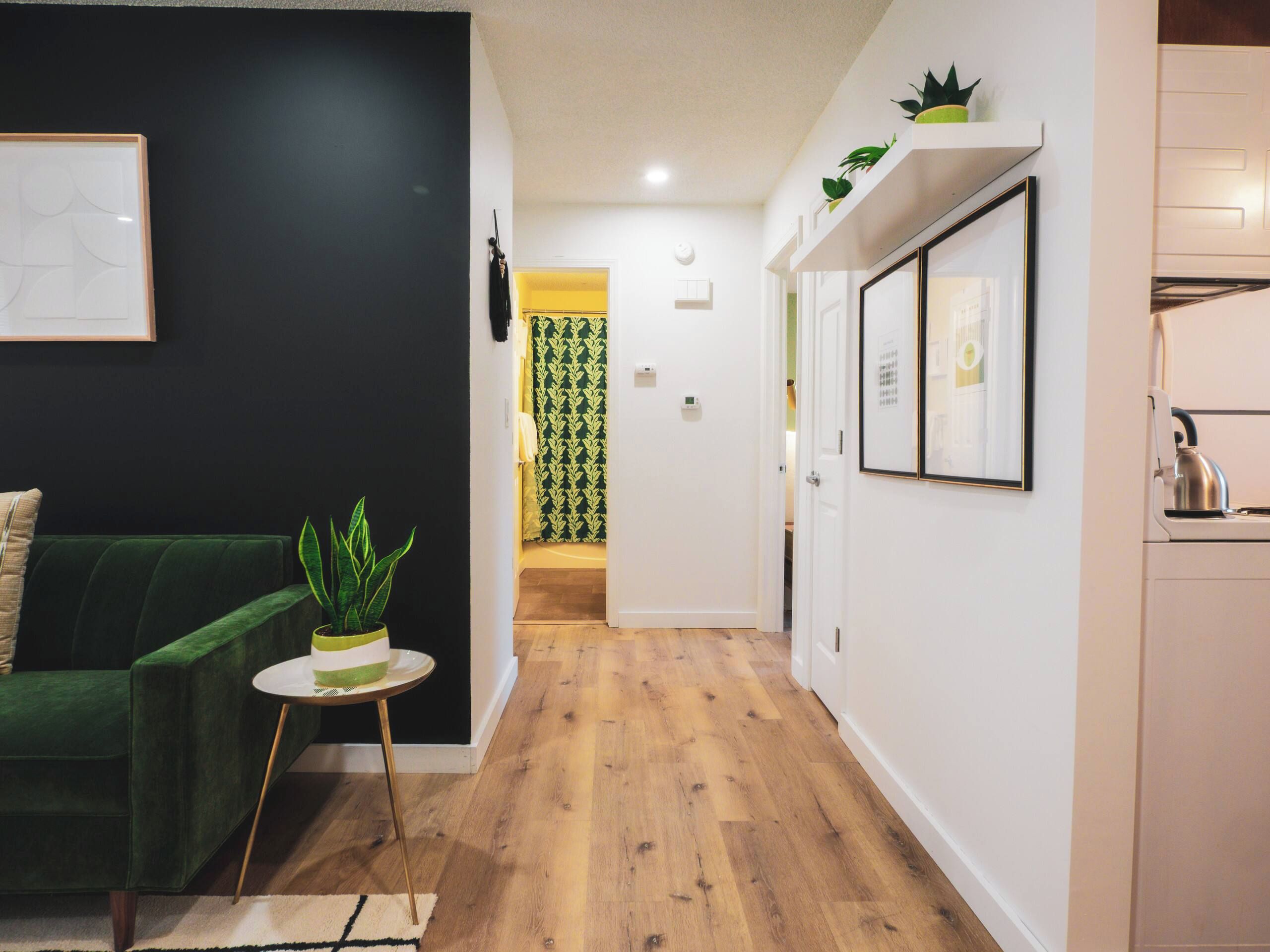 Een moderne woonkamer met een groene bank, een klein rond tafeltje met een plant erop, en een lijst met een foto aan de muur.