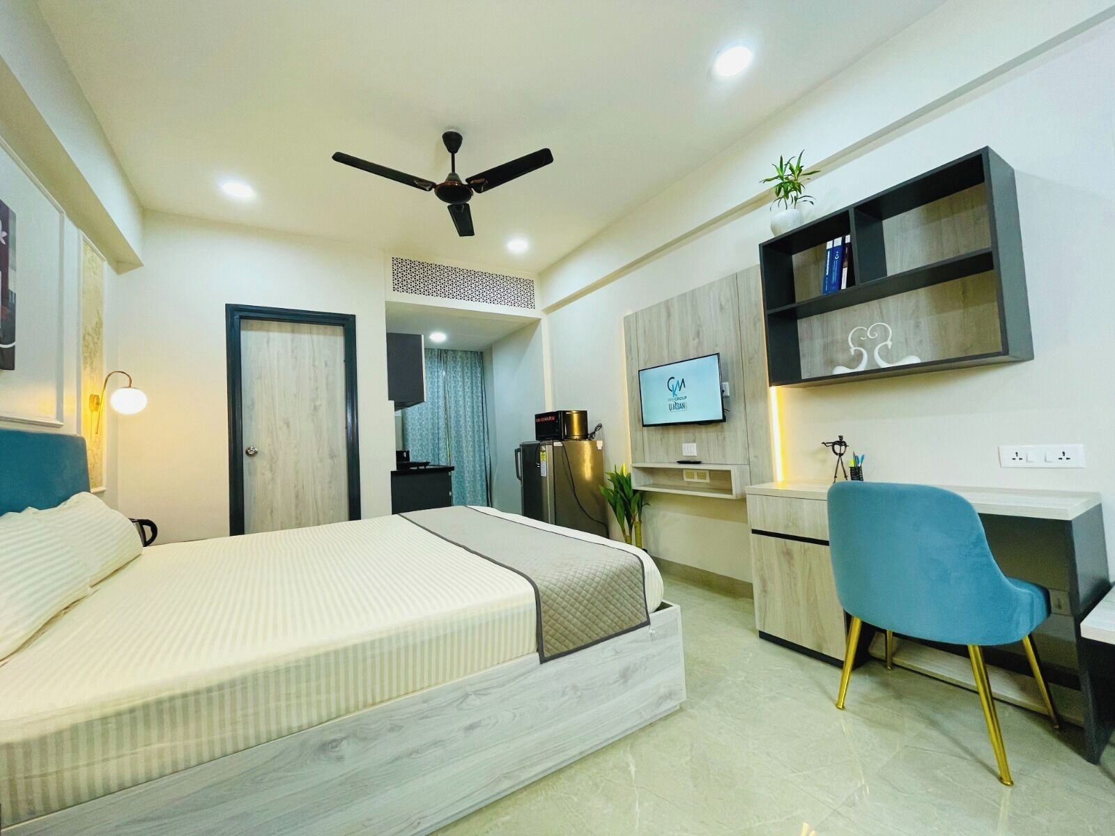 A modern hotel room with a bed, desk, chair, TV, and ceiling fan.