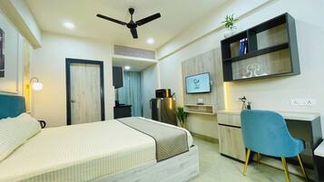 A modern hotel room with a bed, desk, chair, TV, and ceiling fan.
