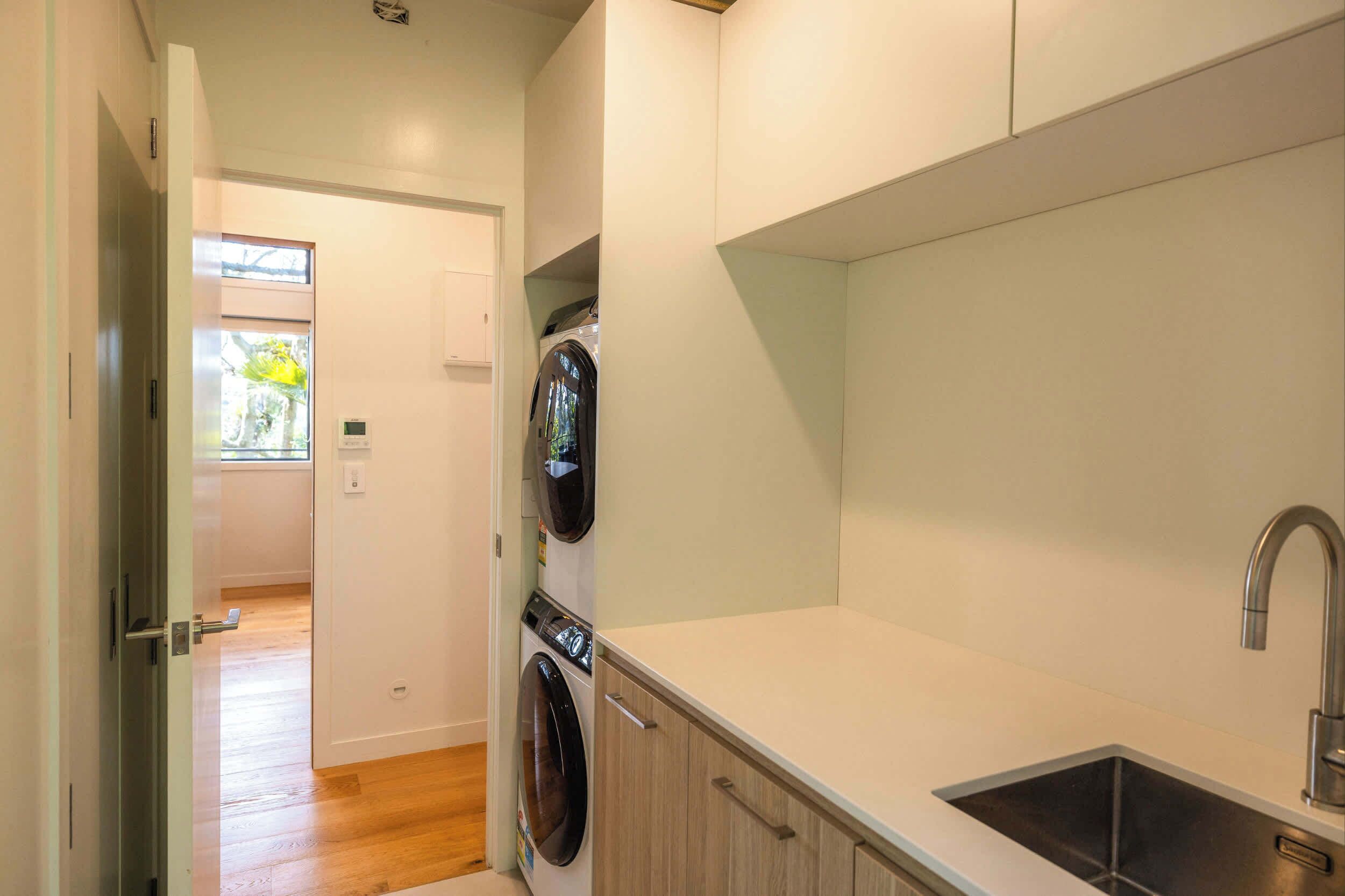 Een kleine keuken met een ingebouwde wasmachine en droger, een spoelbak en een deur naar een andere kamer.