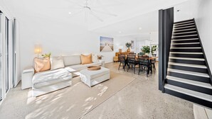 Ein modernes Wohnzimmer mit einem weißen Sofa, einem Essbereich mit Tisch und Stühlen sowie einer Treppe.