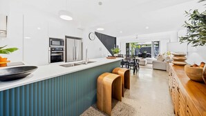 Eine moderne Küche mit einer zentralen Kochinsel, Edelstahlgeräten und einem Essbereich mit einer Couch und einem Tisch.