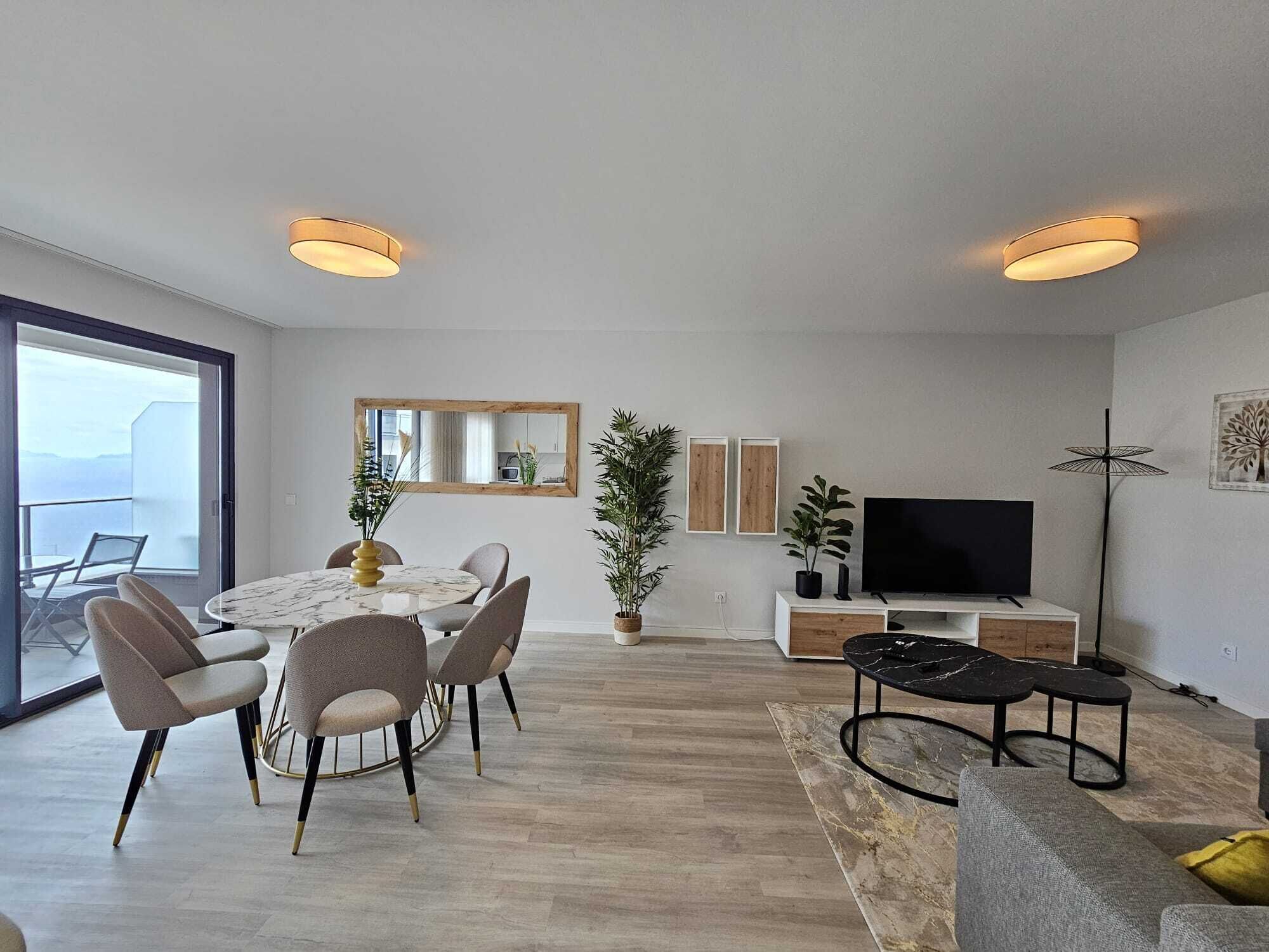 Un salon moderne comprenant un coin repas, un téléviseur à écran plat et une grande fenêtre donnant sur un balcon.