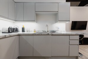 Une cuisine moderne avec des meubles gris, un plan de travail en marbre, un évier encastré et un téléviseur noir fixé au mur.
