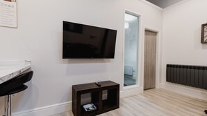 Un saló modern amb televisió de pantalla plana penjada a la paret, una petita taula auxiliar de fusta amb un comandament a distància i un taulell de marbre.