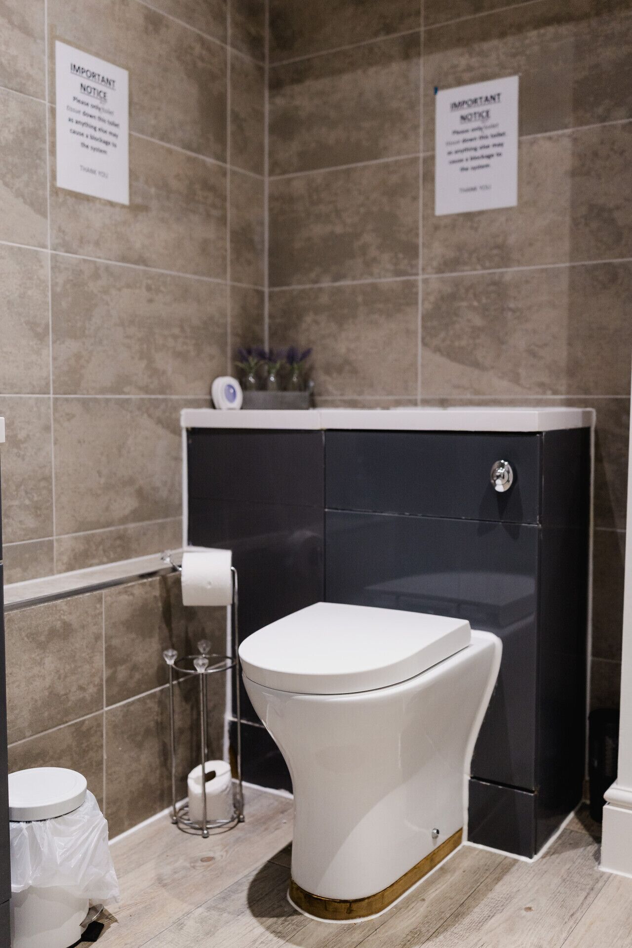 A modern bathroom with a white toilet, black cabinet, and tiled walls. There are two signs on the wall, one above the toilet and one above the cabinet.
