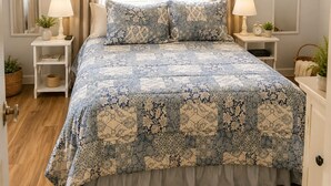Un dormitorio con una cama grande, dos mesitas de noche con lámparas, una lámpara colgante y una ventana con cortinas.