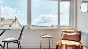 A room with a large window, a chair, a small table with plants, and a radiator.