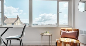 A room with a large window, a chair, a small table with plants, and a radiator.