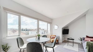 A modern living room with a dining area, large windows, a flat-screen TV, and a cozy seating arrangement.