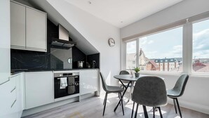 A modern kitchen with white cabinets, a black marble backsplash, and a dining area with two chairs and a table.