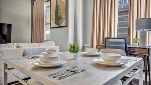 A dining area with a table set for four, a sofa, a TV, and a window with curtains. - Sophisticated Downtown Loft / FREE Parking & Gym (Cleveland)