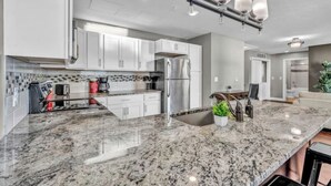 Una cocina moderna con armarios blancos, un refrigerador de acero inoxidable y una encimera de granito.