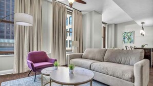 Una sala moderna con un sofá color beige, un sillón morado y una mesa de centro redonda.