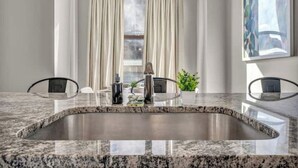 Una cocina moderna con encimera de granito, pileta de acero inoxidable y dos sillas.
