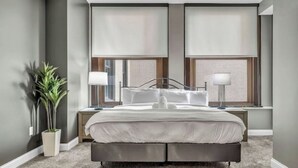 Un dormitorio moderno con una cama grande, dos lámparas de noche, una planta en maceta y vistas al exterior.