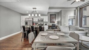 Una cocina moderna con armarios blancos, un refrigerador de acero inoxidable y una zona de comedor con una mesa y sillas grises.