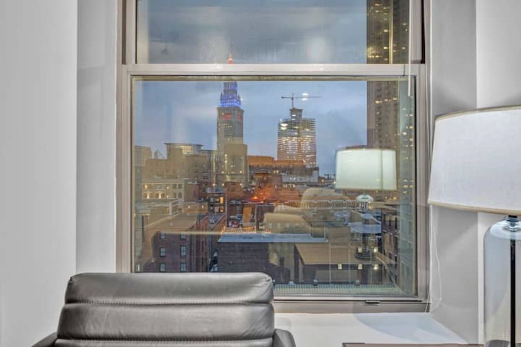 Ein Zimmer mit Blick auf eine Stadtansicht durch ein großes Fenster, ein Sessel und eine Lampe.