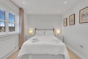 Ein Schlafzimmer mit einem großen Bett, zwei Nachttischen mit Lampen, einem Fenster mit Jalousien und gerahmten Bildern an der Wand.