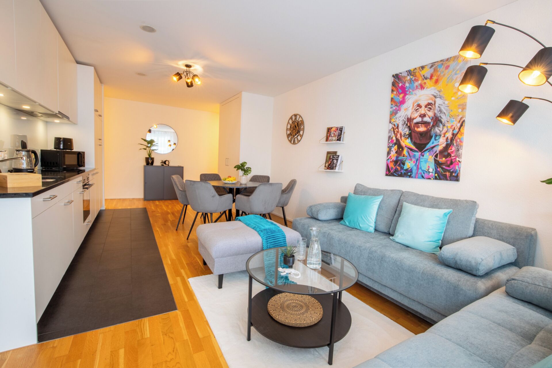 Een moderne woonkamer met een grijze bank, een glazen salontafel en een eethoek met grijze stoelen.