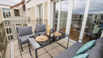 A balcony with a sofa, chairs, and a table with decorative items.