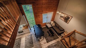 A high-ceilinged room with a dining area, a sofa, and a window overlooking a forest. - Aurelfox Chalet A2 by Aavalevi (Levi)