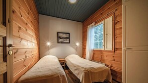 A cabin-style room with two single beds, wooden walls, a window with blinds, and a framed picture on the wall. - Aurelfox Chalet A2 by Aavalevi (Levi)