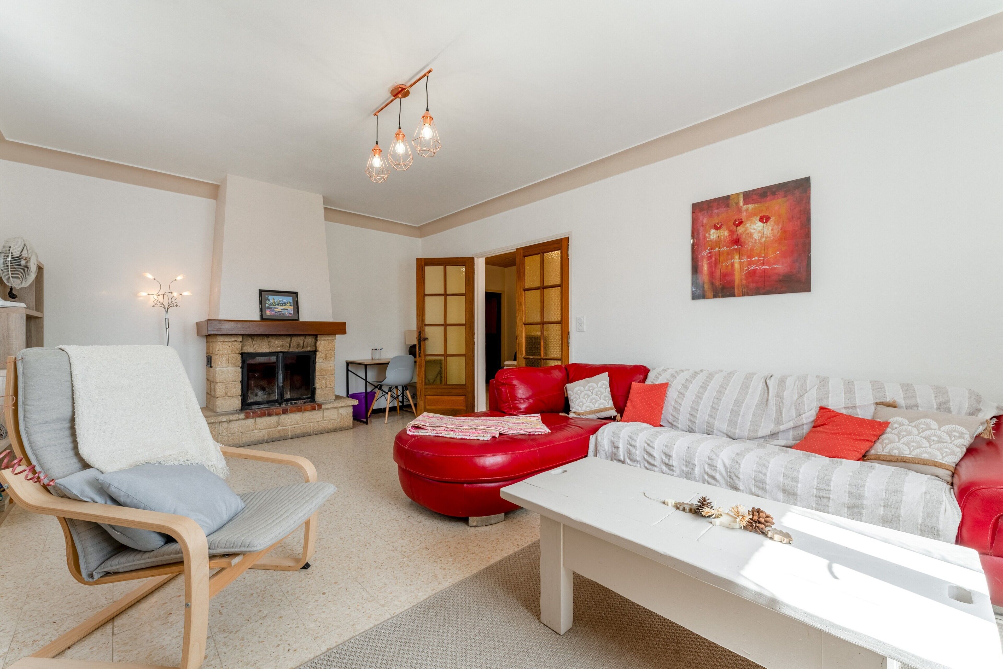 Een woonkamer met een open haard, een rode bank, een witte tafel en een rode fauteuil.