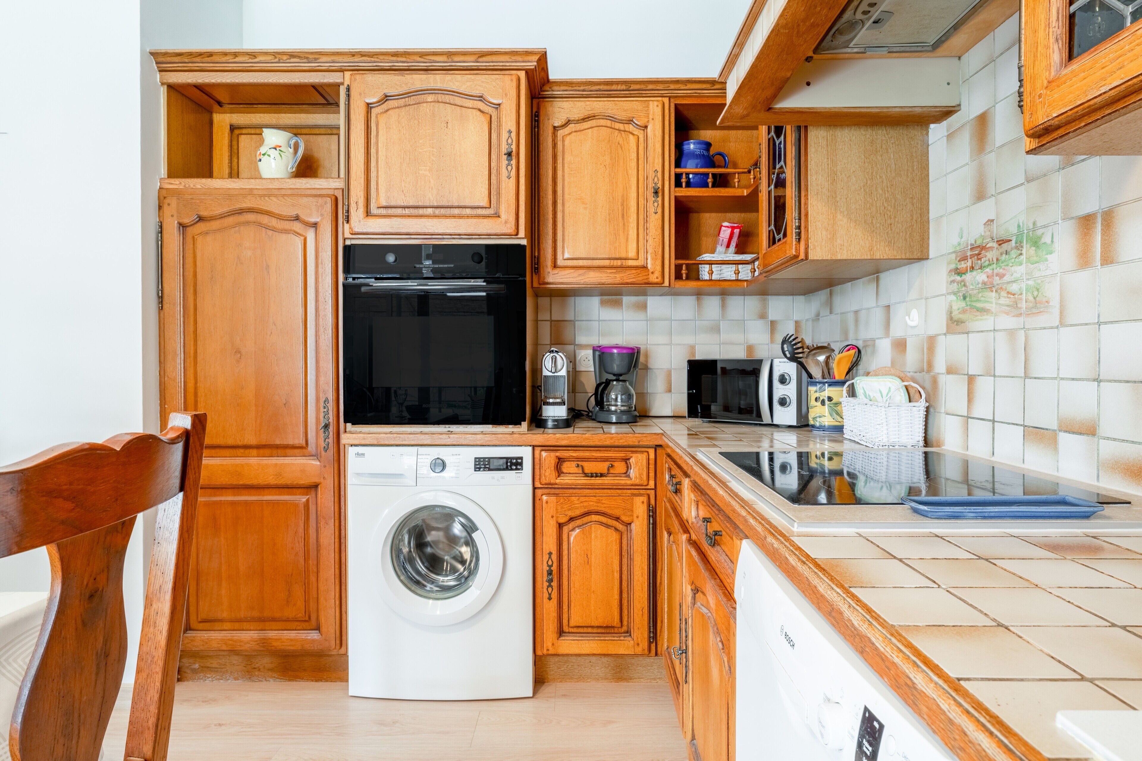 A compact kitchen with wooden cabinets, a washing machine, a coffee maker, and a microwave.