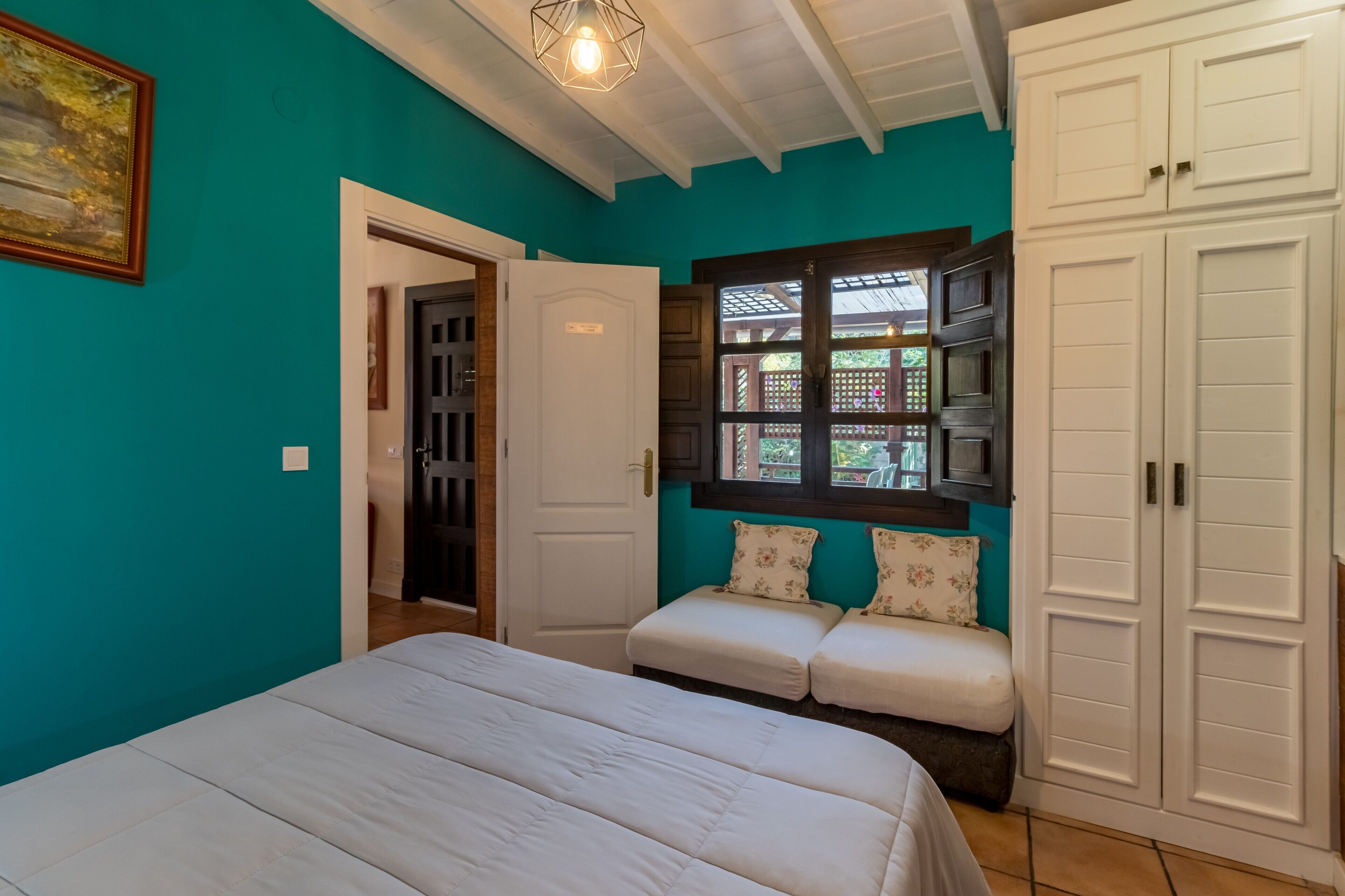 Une chambre à coucher avec un lit, un banc, une armoire et une fenêtre donnant sur un beau paysage.