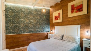 A bedroom with a large bed, wooden paneling, a window, and a wall-mounted light fixture. - Rural House 'El Capricho de Rosmary' with Mountain Views and Private Garden (Villanueva)