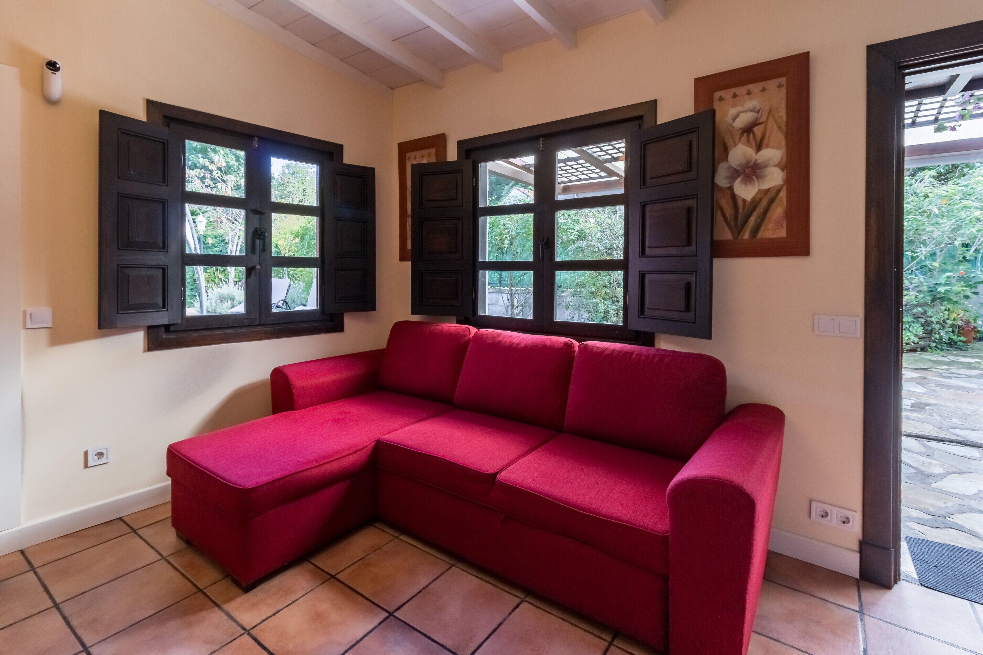 Un sofá seccional rojo en una habitación con dos ventanas, una puerta y un cuadro colgado en la pared.
