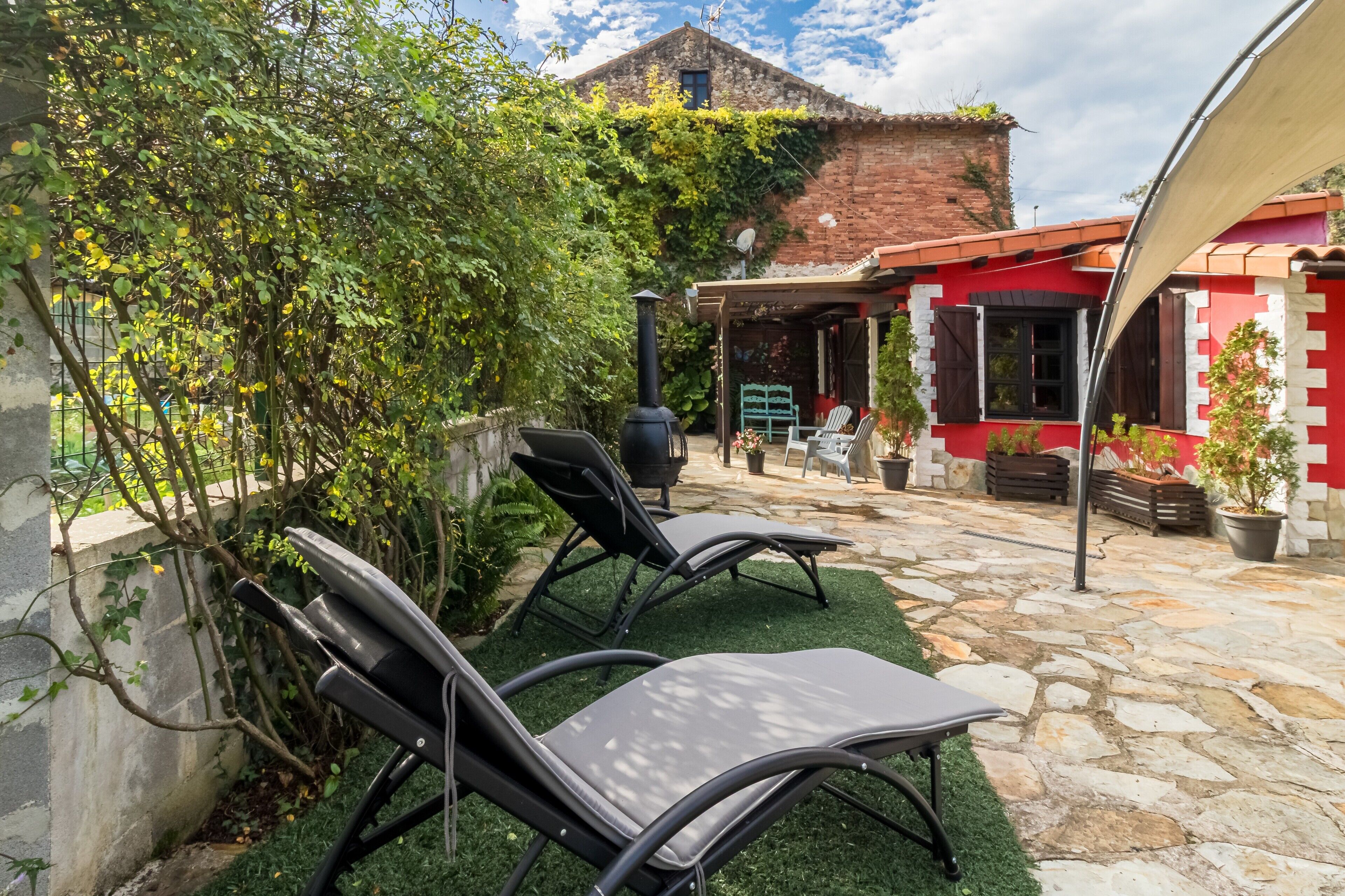Un patio con dos sillones de descanso, un sendero de piedra, un edificio de ladrillo y una zona cubierta con una mesa y sillas.
