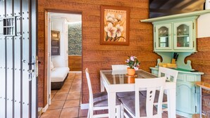 A room with a wooden wall, a dining table with chairs, a cabinet with glass doors, and a television mounted on the wall. - Rural House 'El Capricho de Rosmary' with Mountain Views and Private Garden (Villanueva)