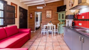 A compact living space with a red sofa, a dining table, a kitchen area with a microwave, and a red tiled backsplash. - Rural House 'El Capricho de Rosmary' with Mountain Views and Private Garden (Villanueva)