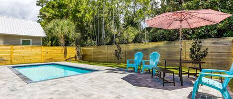 A backyard with a swimming pool, patio furniture, and a wooden fence.