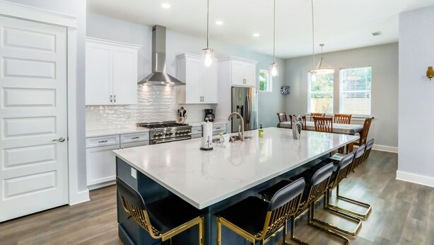 Una cocina moderna con armarios blancos, una isla grande con taburetes de bar, electrodomésticos de acero inoxidable e iluminación colgante.