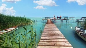 A wooden pier extending into a clear blue lagoon with boats docked on either side. - TópART Apartman I: Apartment with terrace (Balatonfenyves)