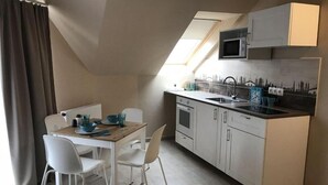 A compact kitchen with a microwave, sink, and white cabinetry. There is a dining table with chairs and a window providing natural light. - TópART Apartman I: Apartment with terrace (Balatonfenyves)
