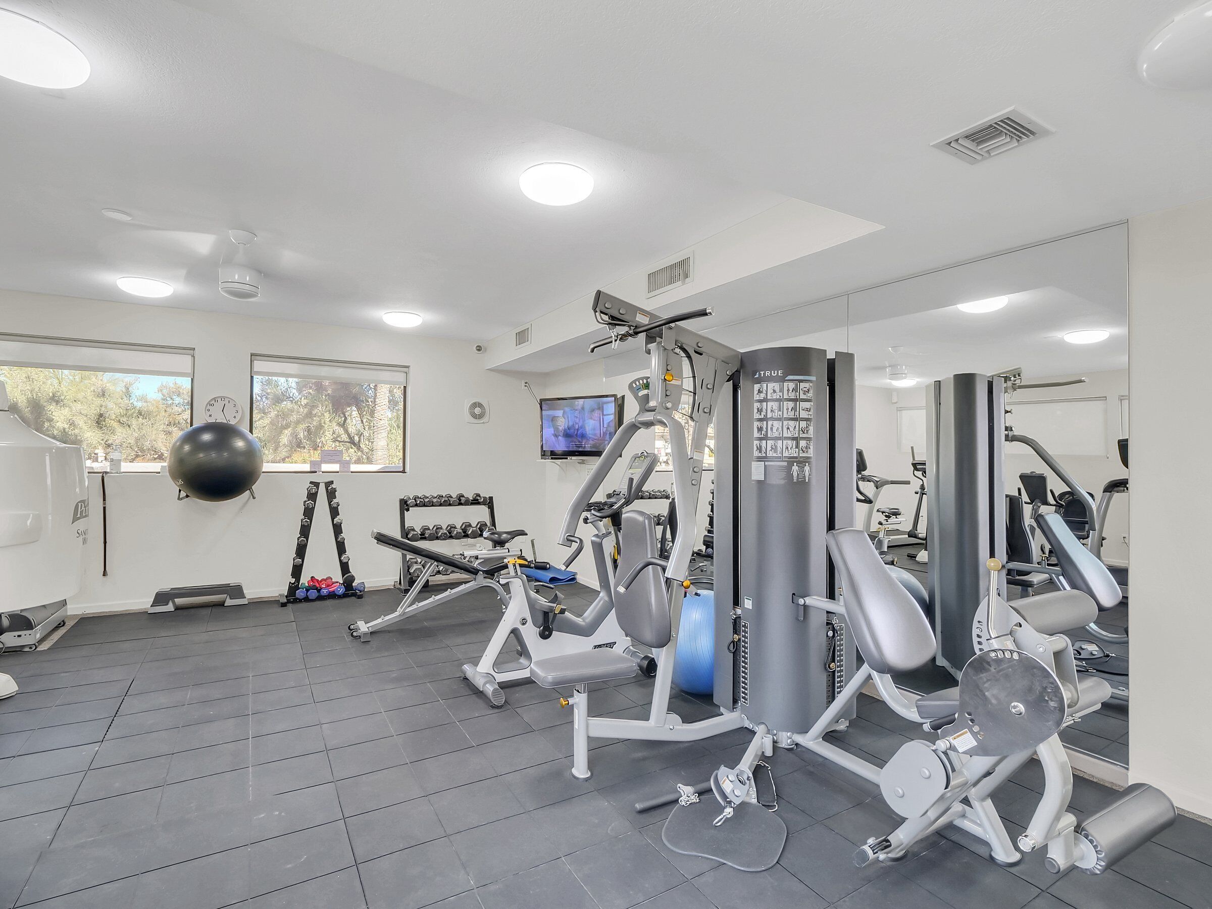 A gym with various exercise equipment, a clock, and a TV on the wall.