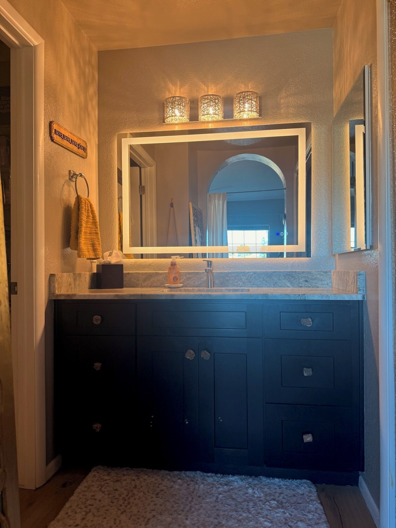 A bathroom with a dark wooden vanity, a large mirror, and three lit sconces above the mirror.