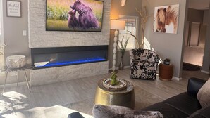 A modern living room with a flat-screen TV mounted on a brick wall, a fireplace with a blue-lit water feature, a patterned armchair, and a decorative vase. - STUNNING Views, SUBERB Location..NEW NEW NEW to The Racquet Club in Scottsdale! (Scottsdale)