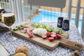 Ett bord med en träbricka som innehåller skivade tomater, mozzarella och grönsaker, ett glas vitt vin och två saltströare med ankarmotiv.