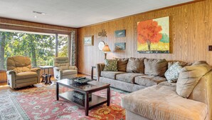 A living room with a large window, a sofa, a coffee table, and a patterned rug. - Private Yard & Grill: Retreat Near Norfolk Lake! (Mountain Home)