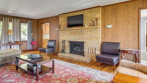 A living room with a stone fireplace, a television mounted above it, and a red patterned rug. - Private Yard & Grill: Retreat Near Norfolk Lake! (Mountain Home)