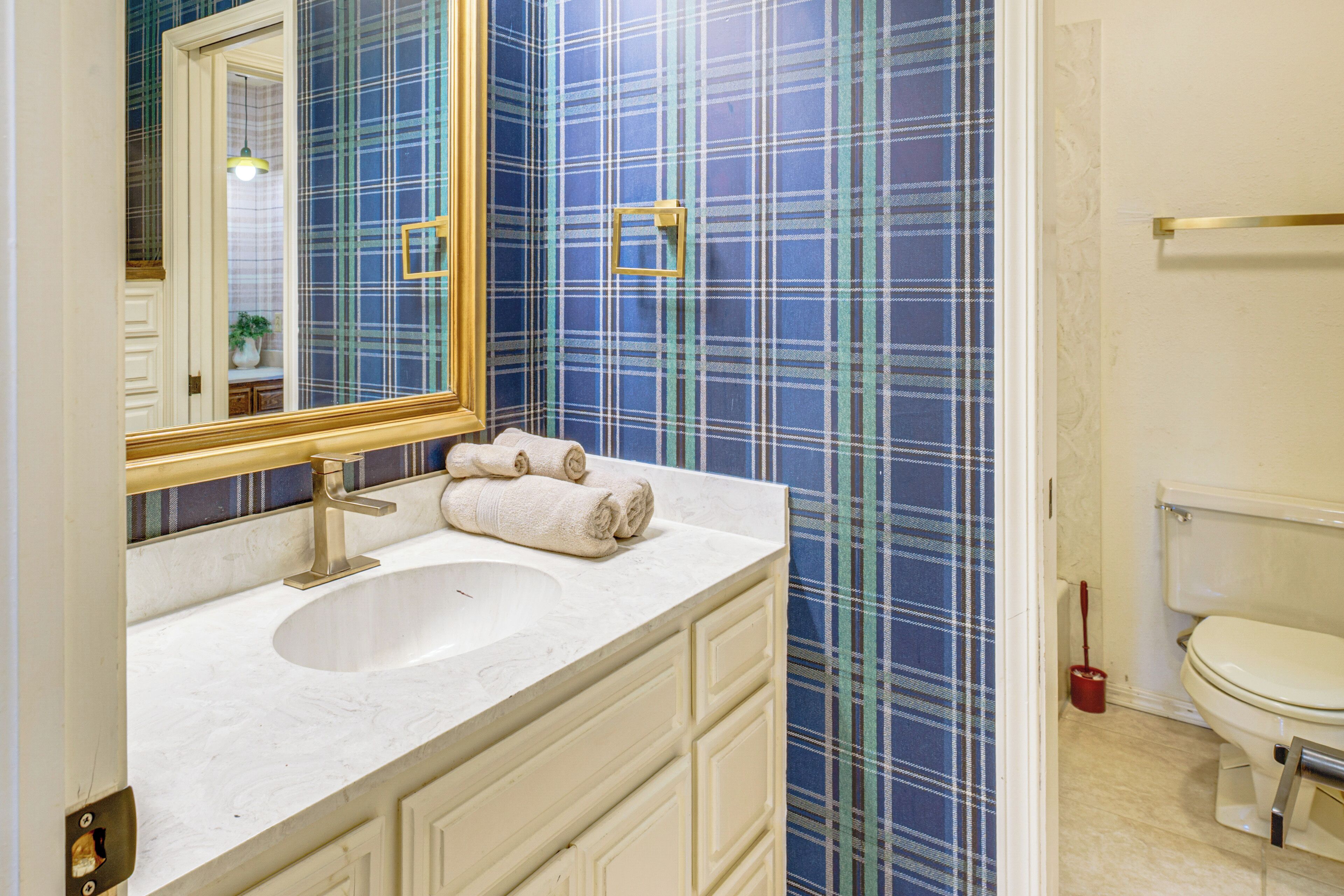 A bathroom with a white sink, a mirror, and a toilet. The walls have a blue plaid wallpaper.