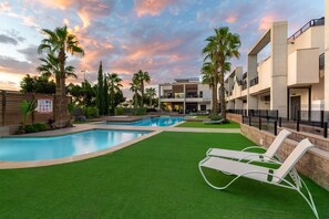 A resort pool area with artificial grass, lounge chairs, and palm trees. - Laguna Rocher by Fidalsa (Guardamar del Segura)