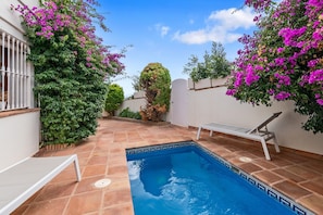 Una piscina con borde de baldosas, rodeada de vegetación exuberante y plantas en flor.