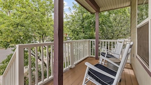A wooden deck with white railings, two white rocking chairs, and a view of green trees. - NAU/DT | Elevated 2 bdrm | AC | Dog Friendly (Flagstaff)